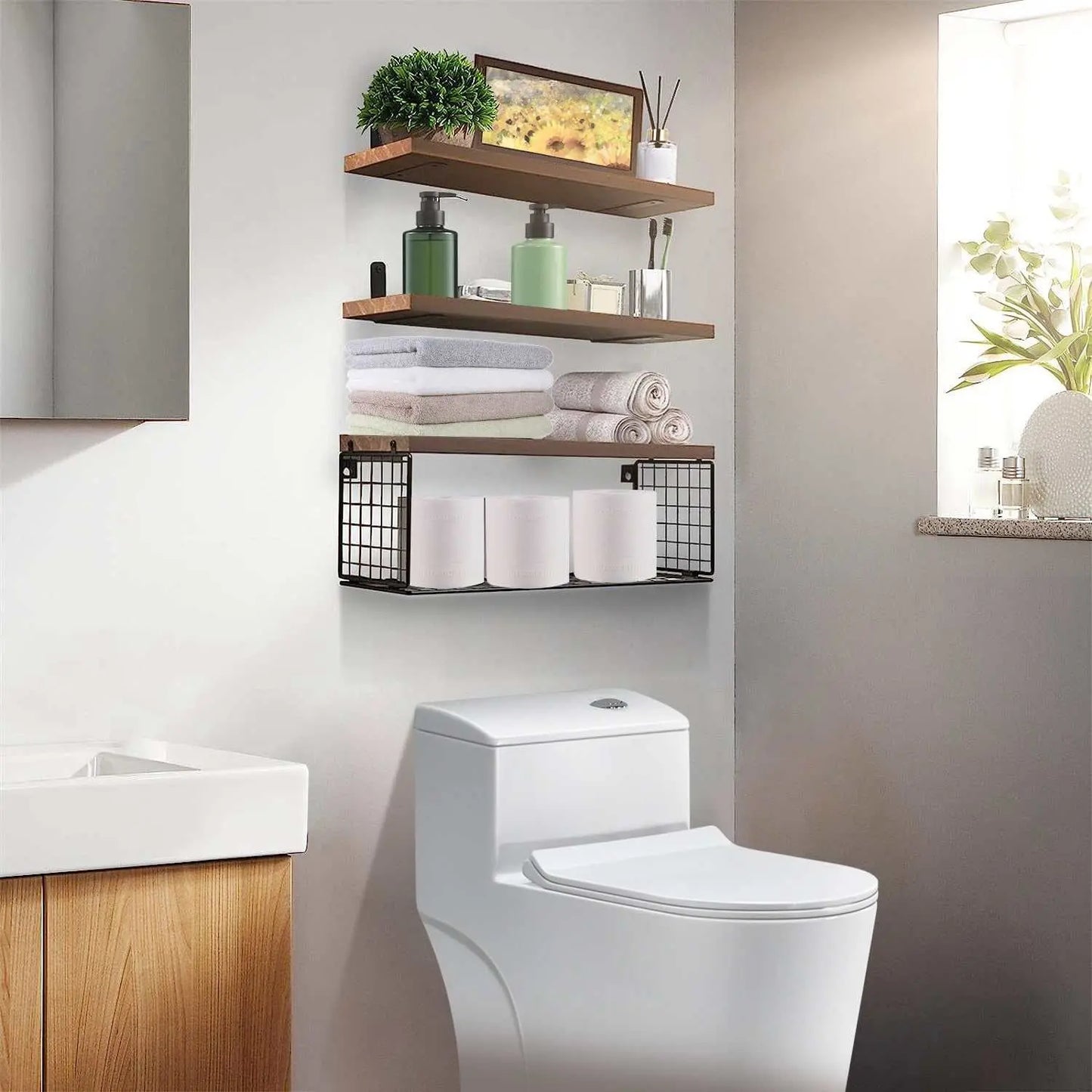 Brown wooden floating shelves with black storage basket mounted on bathroom wall holding toiletries, towels, and toilet paper.