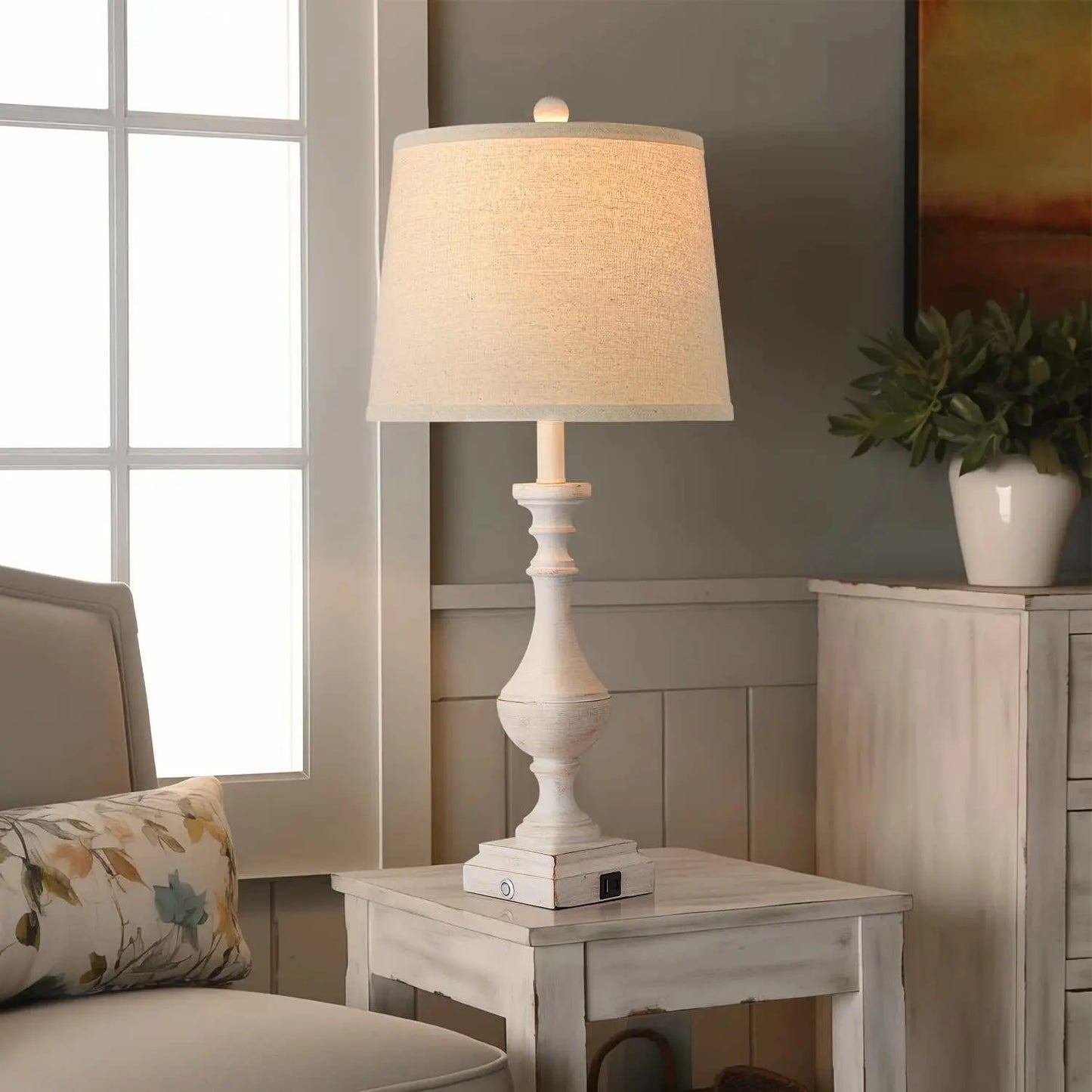 Coastal candlestick table lamp with distressed white finish and beige linen shade on rustic wooden side table in living room setting