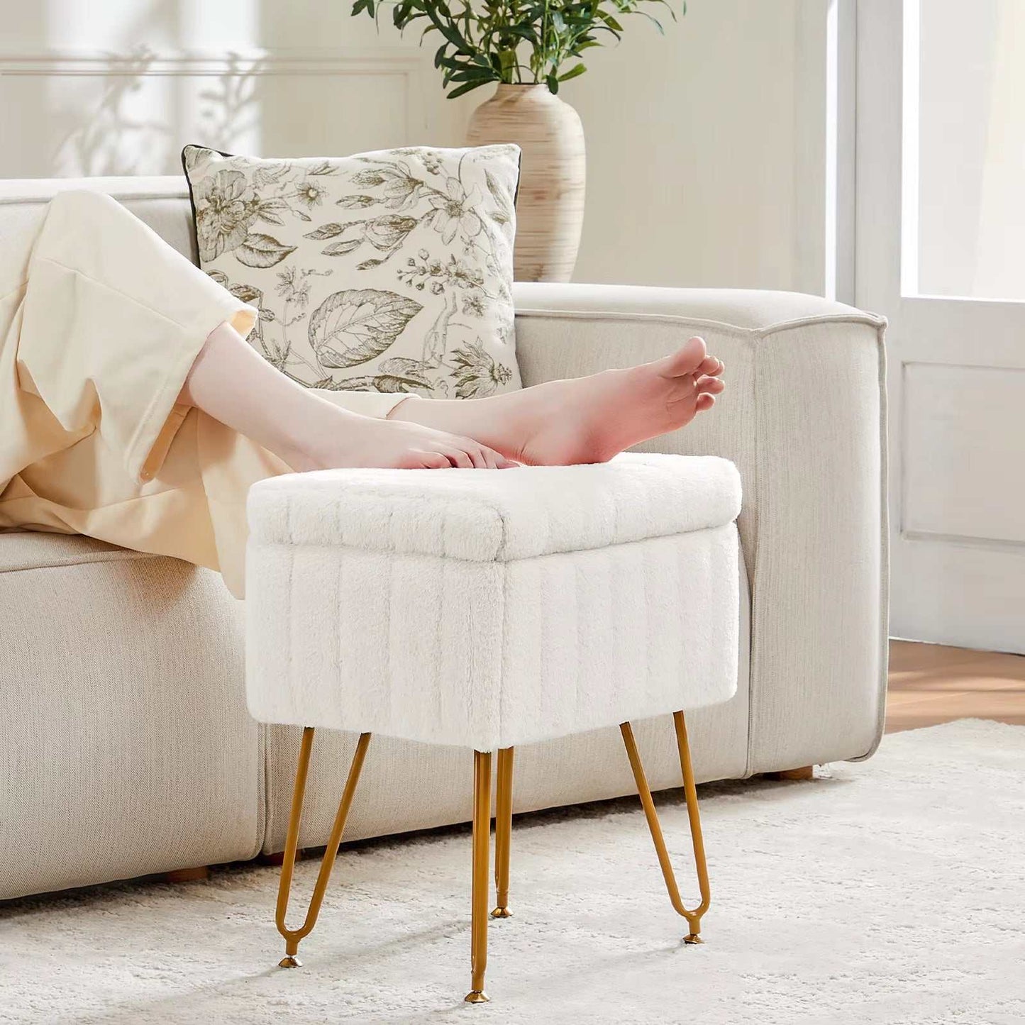 White faux fur living room ottoman with gold metal legs and hidden storage, used as a footrest next to a beige sofa