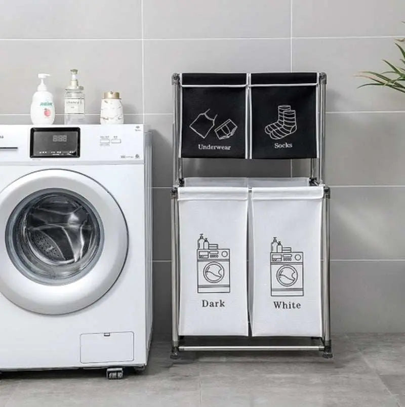Two-tier laundry hamper with four removable labeled bags for sorting underwear, socks, darks, and whites next to a washing machine in a laundry room