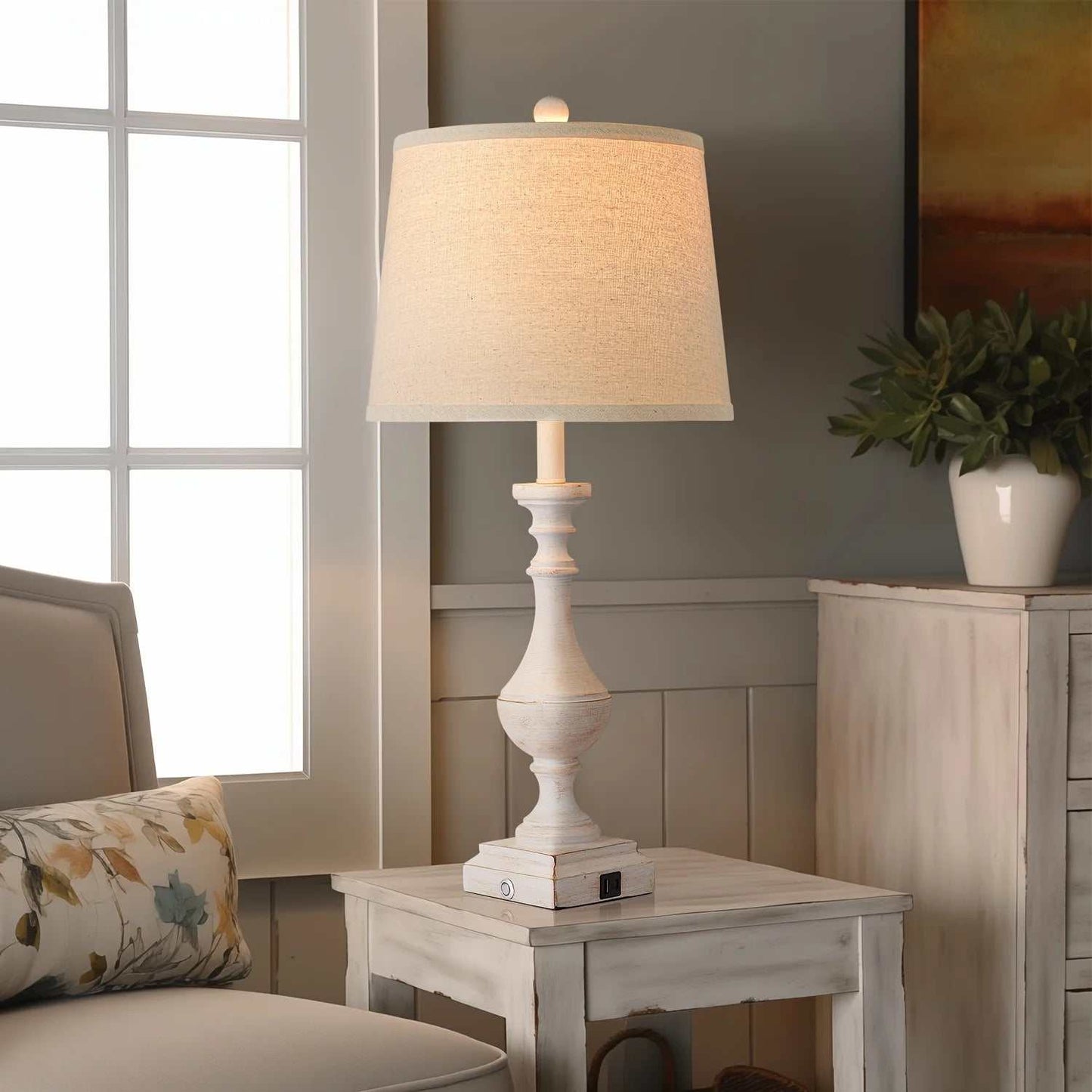 Coastal candlestick table lamp with distressed white finish and beige linen shade on rustic wooden side table in living room setting