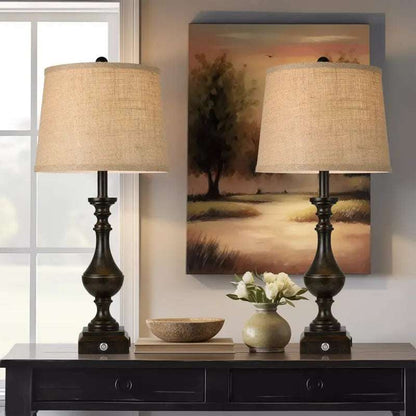 Pair of coastal candlestick table lamps with beige linen drum shades and dark wooden bases on a black console table.