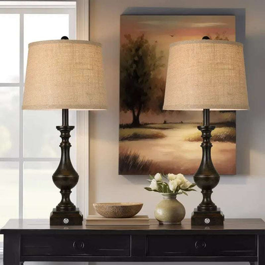 Pair of coastal candlestick table lamps with beige linen drum shades and dark wooden bases on a black console table.