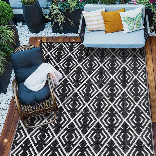 Black and white geometric outdoor patio rug on wooden deck with chair and sofa seating