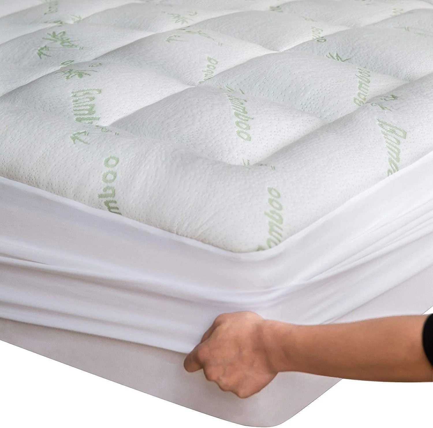 Close-up of a hand fitting a soft, quilted bamboo mattress topper on a twin mattress with breathable, cooling fabric.