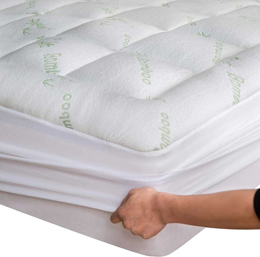 Close-up of a hand fitting a soft, quilted bamboo mattress topper on a twin mattress with breathable, cooling fabric.