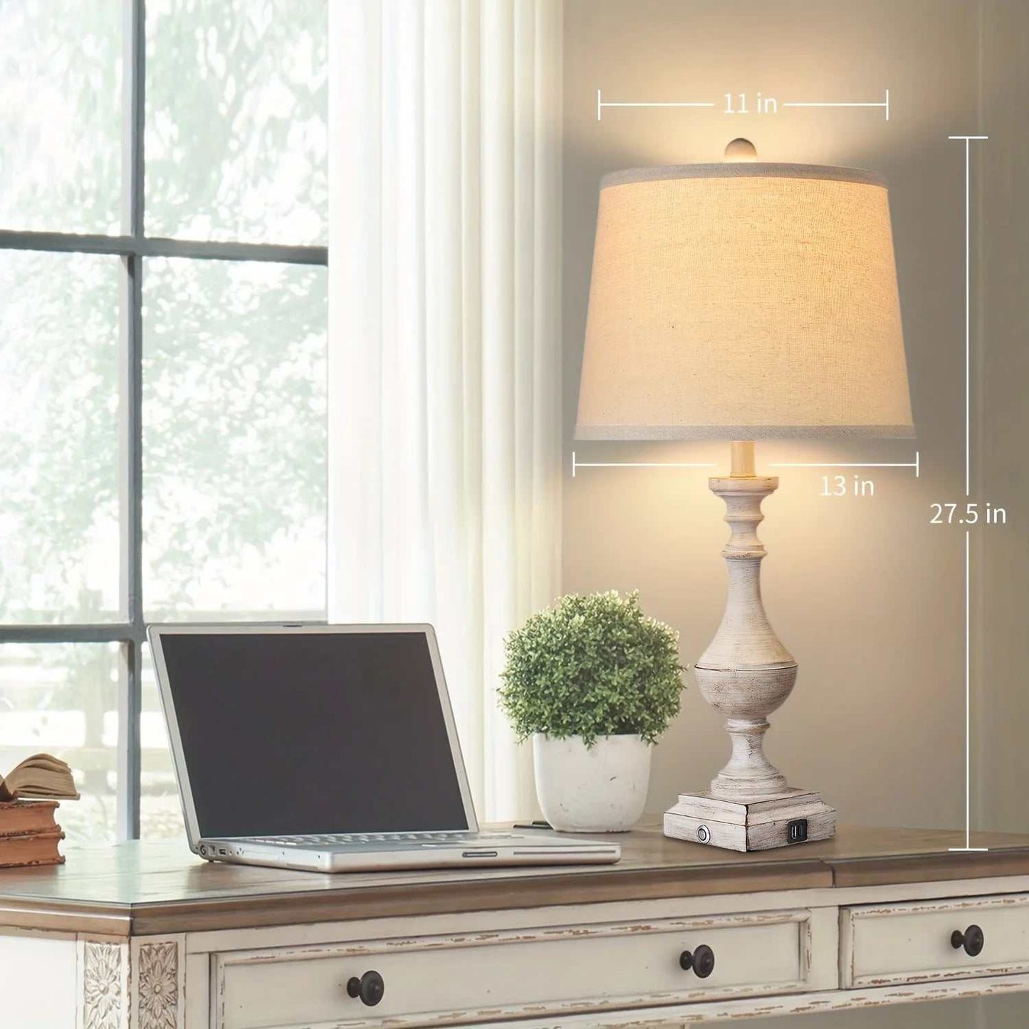 Coastal candlestick table lamp with distressed white finish and linen drum shade on wooden desk next to laptop and plant.
