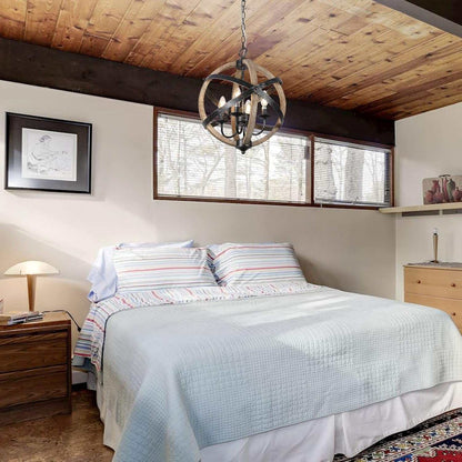 Rustic farmhouse chandelier lamp with wooden sphere frame and black metal chain hanging above bed in cozy bedroom with wooden ceiling and natural light windows