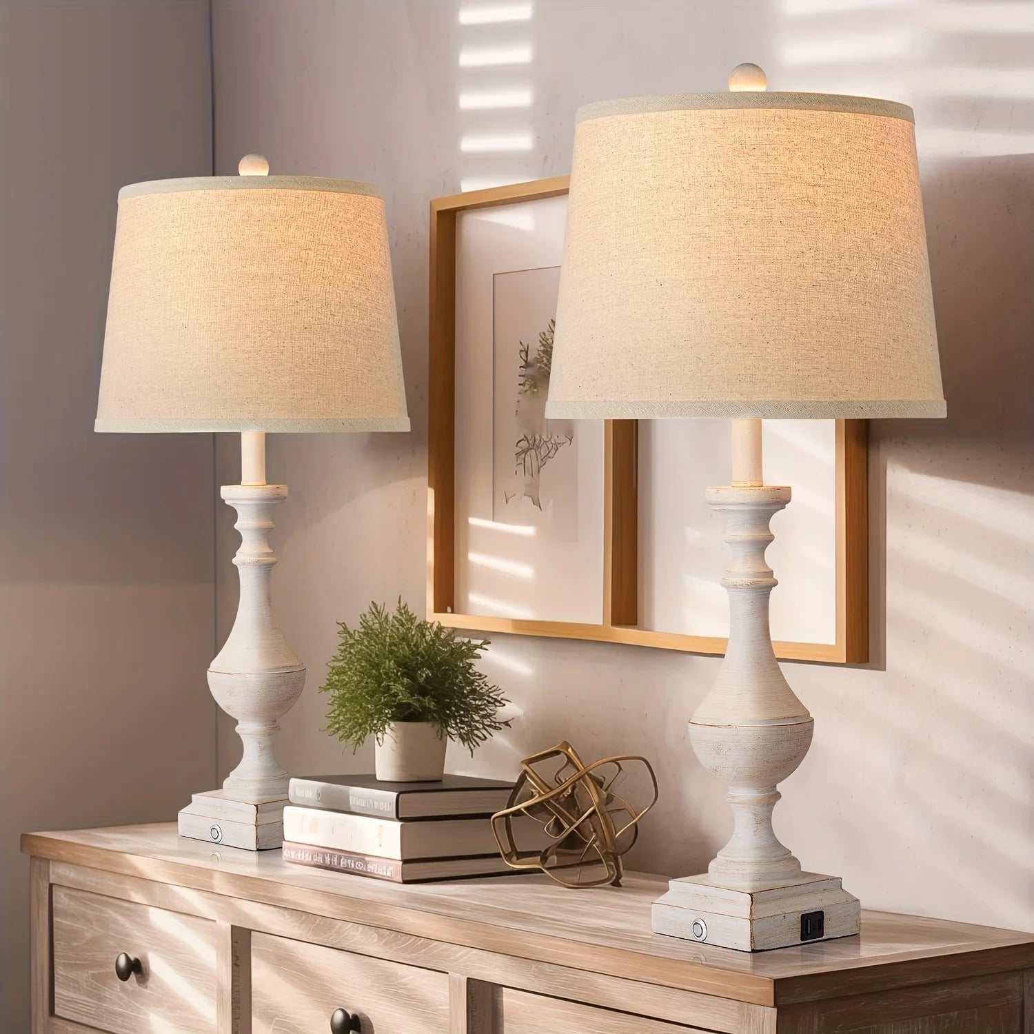 Pair of coastal candlestick table lamps with distressed white finish and beige drum shades on wooden sideboard